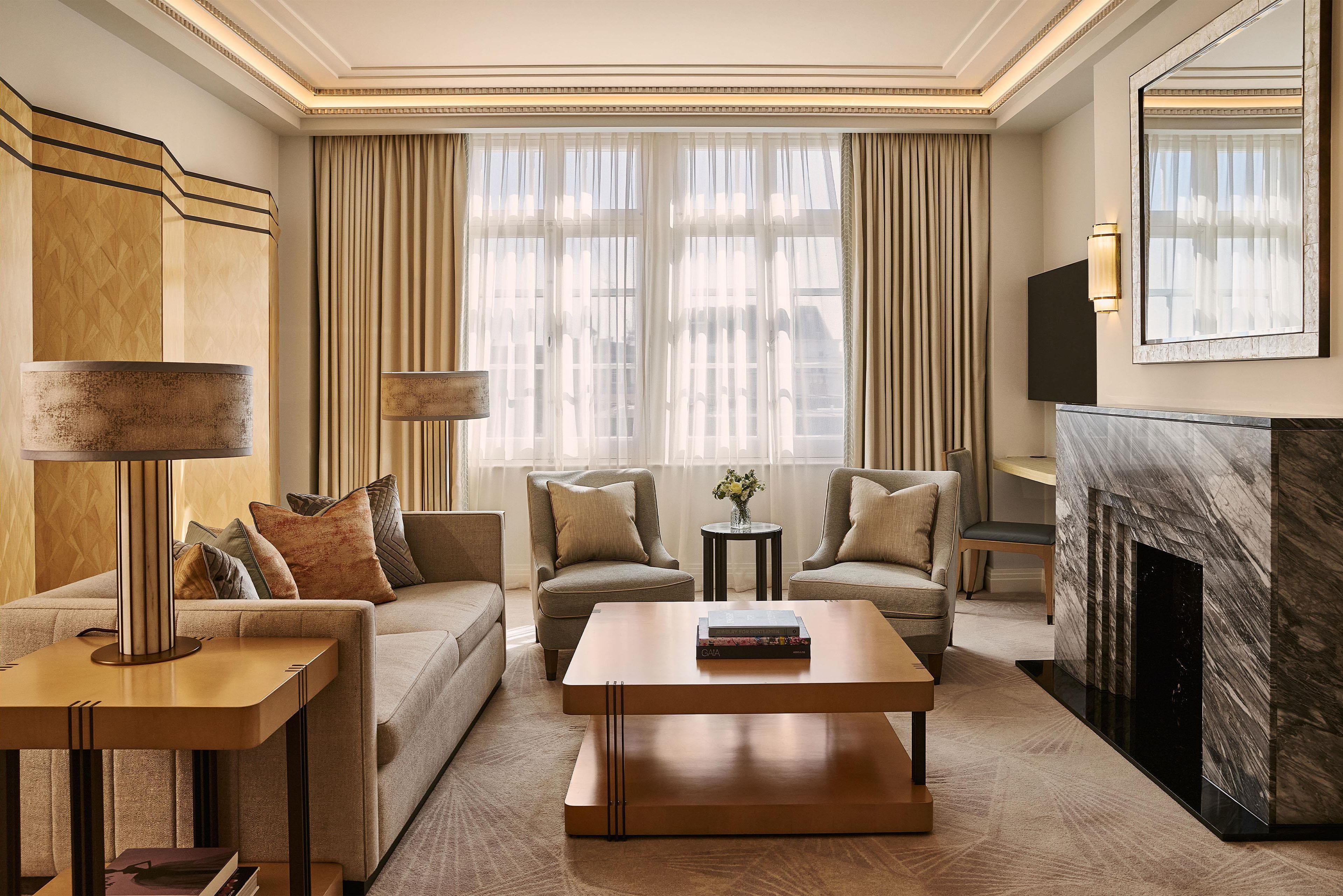 A modern living room with a sofa, two armchairs, a coffee table, a side table, a lamp, a fireplace, and a large window with curtains.