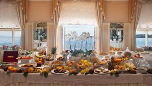 A buffet table with a variety of food items and a scenic view of the sea through large windows. - Grand Hotel Gardone Riviera (Gardone Riviera)