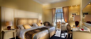 A hotel room with a large bed, two bedside tables, a chair, a desk with a mirror, and a view of the outdoors.