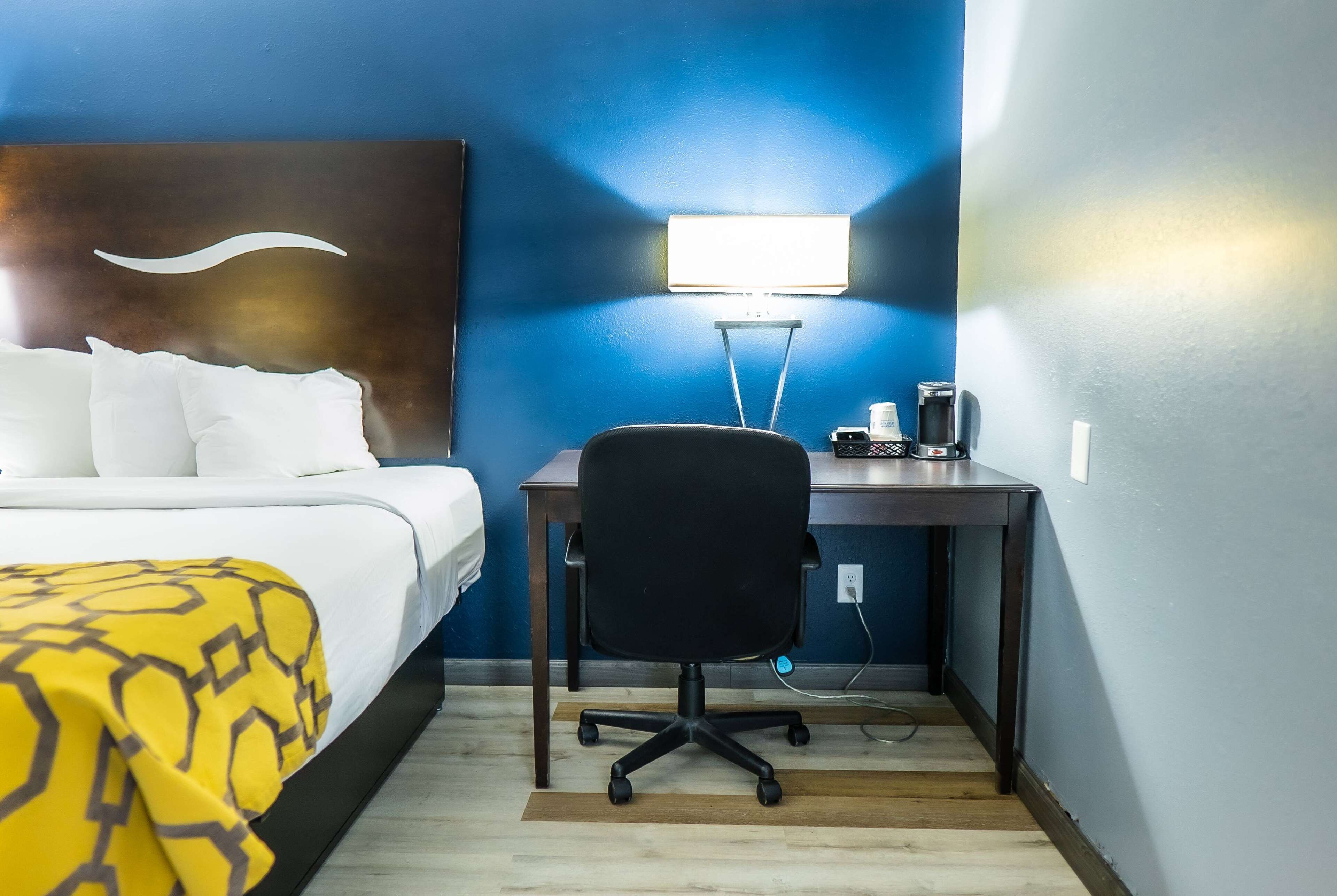 A hotel room with a bed, a desk, a chair, and a nightstand.