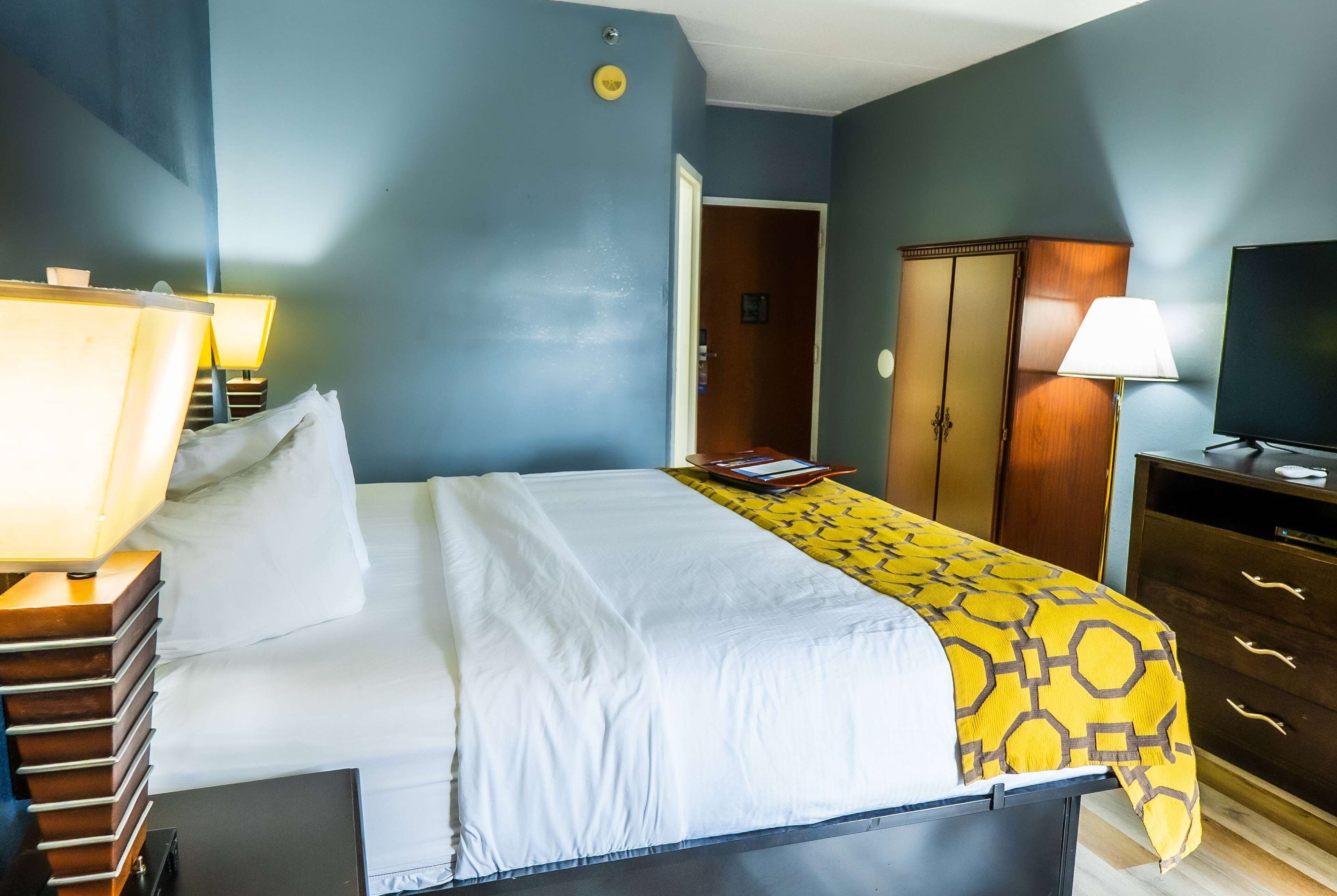 Habitación de hotel con cama, lámparas de noche, armario, televisor y una puerta que da a otra habitación.