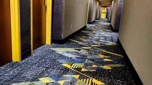 Un couloir d’hôtel avec un tapis à motifs, des portes jaunes et un long couloir.