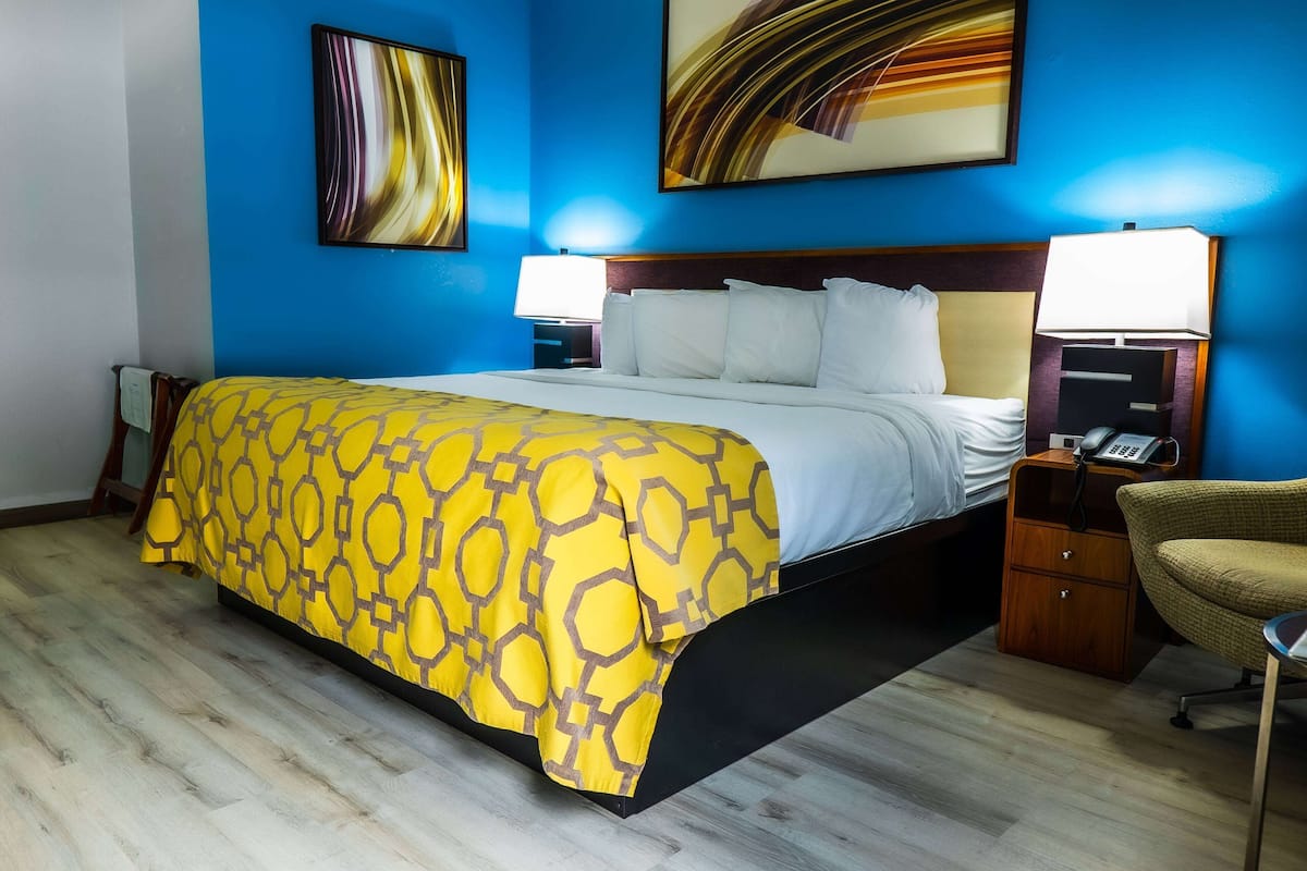 A hotel room with a large bed, two bedside tables with lamps, a chair, and artwork on the walls.