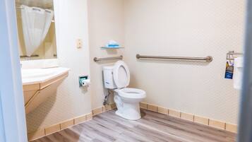 Un baño con inodoro, barandilla, repisa con artículos de aseo y cortina de ducha.