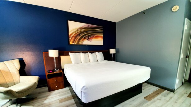 Une chambre d’hôtel avec un grand lit, une chaise, une table de chevet et une lampe fixée au mur.