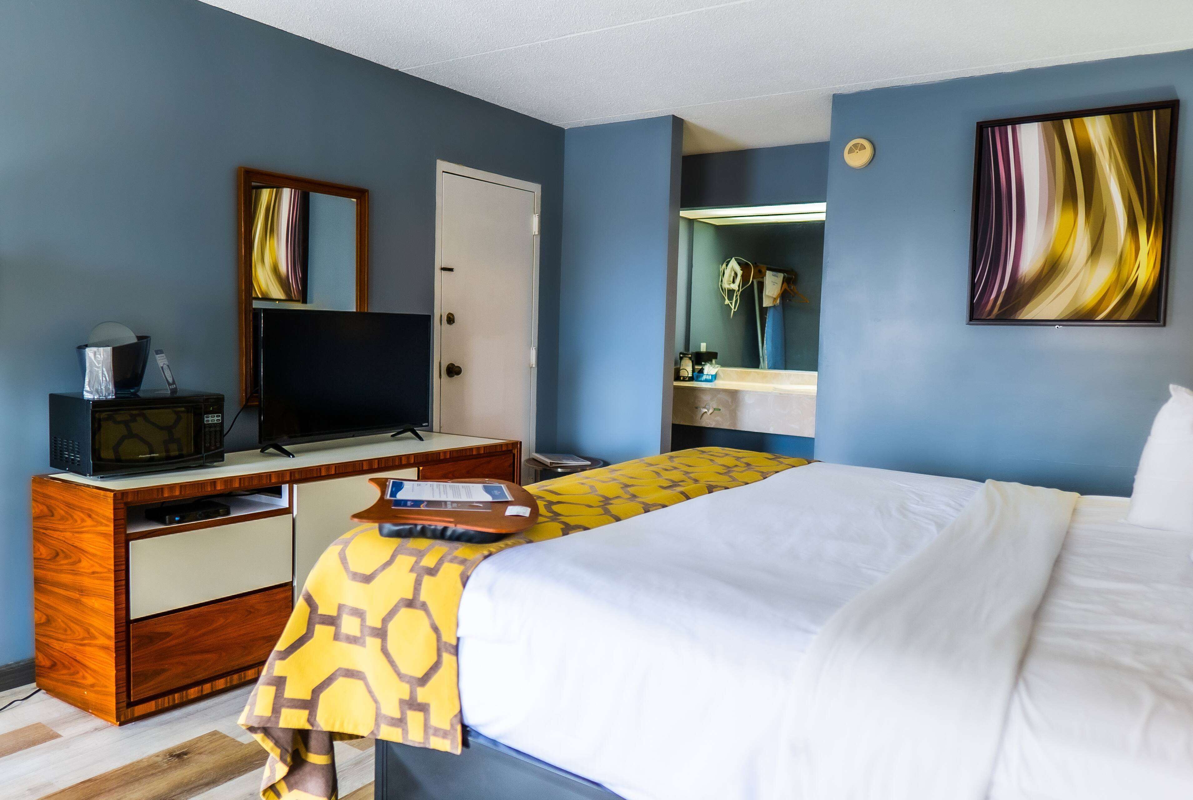 A hotel room with a bed, a desk with a computer and a television, a mirror, and a bathroom with a towel rack.