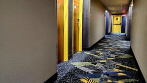 Un couloir d’hôtel avec un sol à motifs, des portes jaunes et un plafond carrelé.