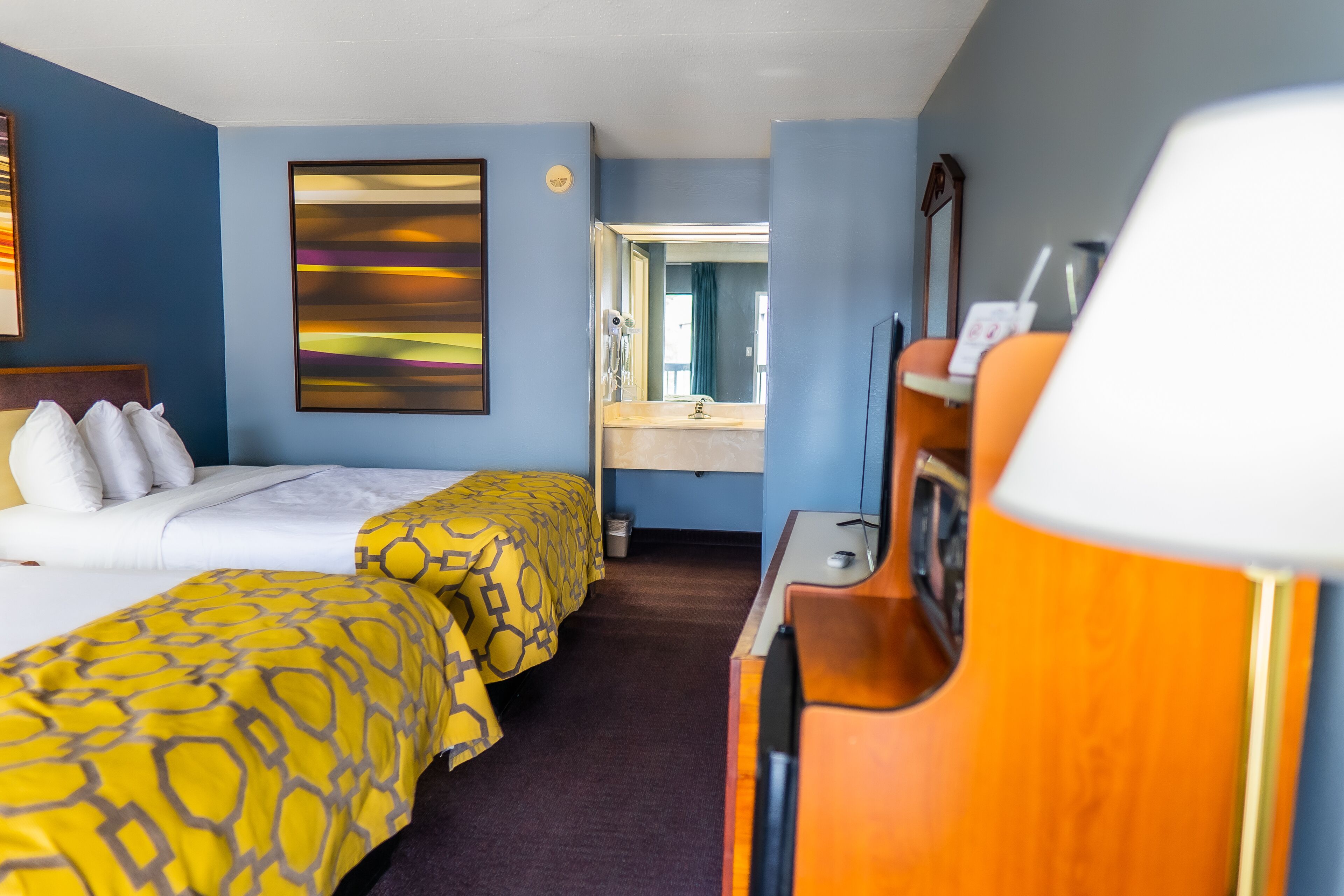 A hotel room with two beds, a desk, a mirror, and a painting on the wall.