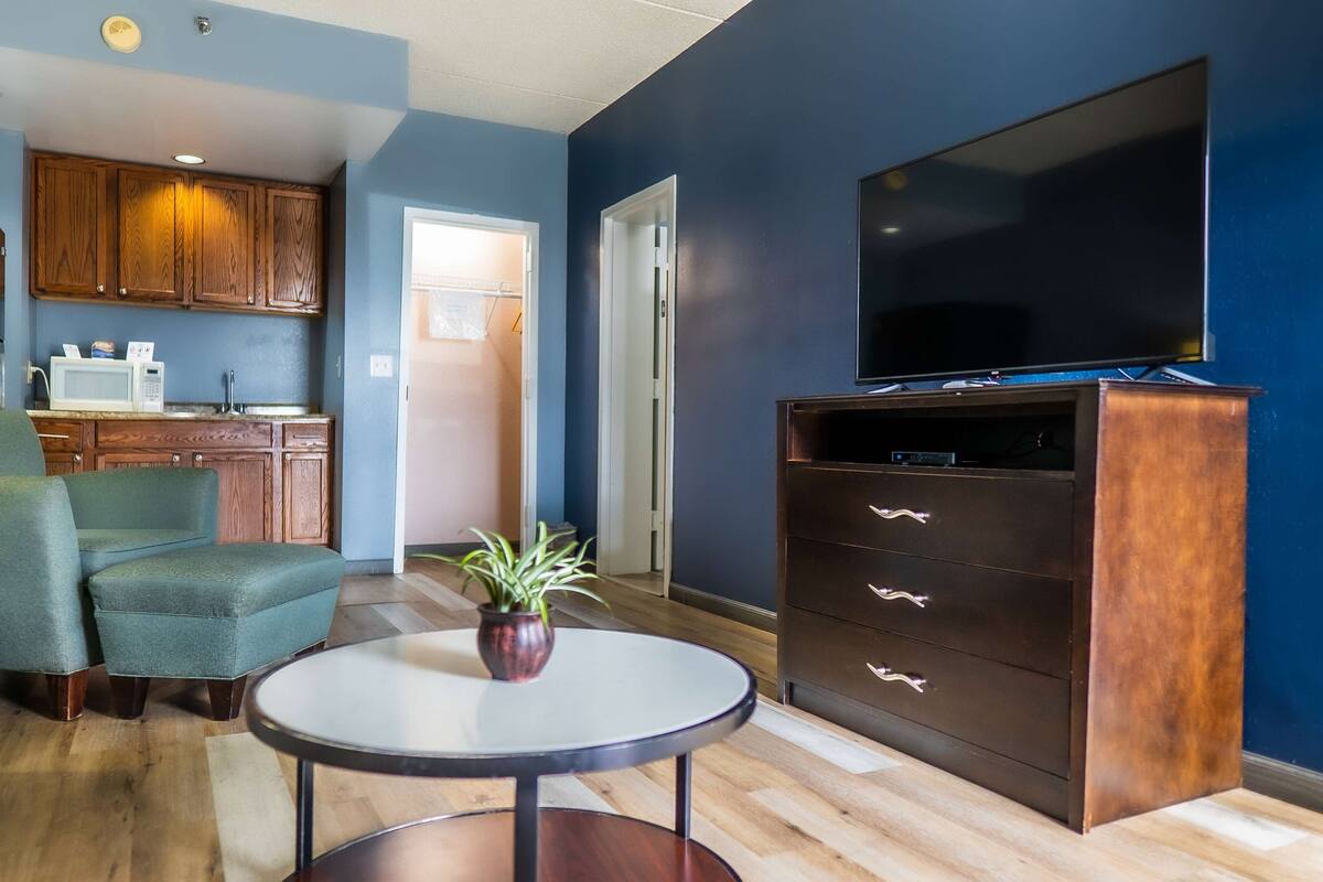 A living room with a TV, wooden cabinets, a dining area, and a kitchen.