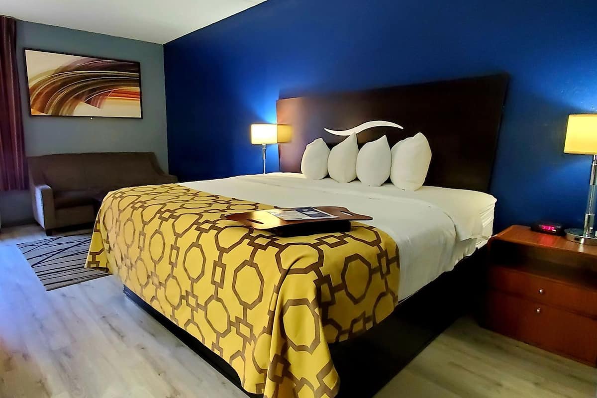 A hotel room with a bed, a nightstand, a lamp, a chair, and a painting on the wall.
