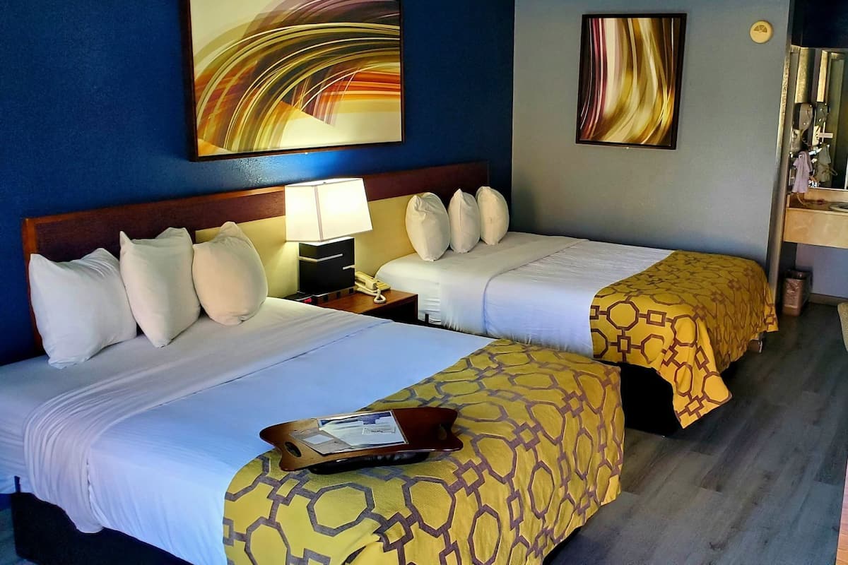A hotel room with two beds, a nightstand with a lamp, a tray table, and artwork on the walls.