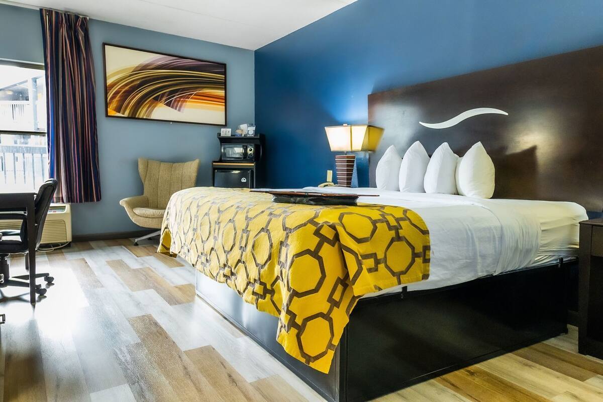 A hotel room with a bed, a desk, a chair, a lamp, and a window with curtains.