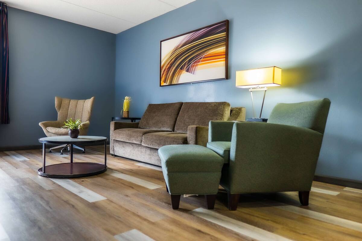 A modern living room with a blue wall, a brown sofa, a green armchair, a round coffee table, and a floor lamp.