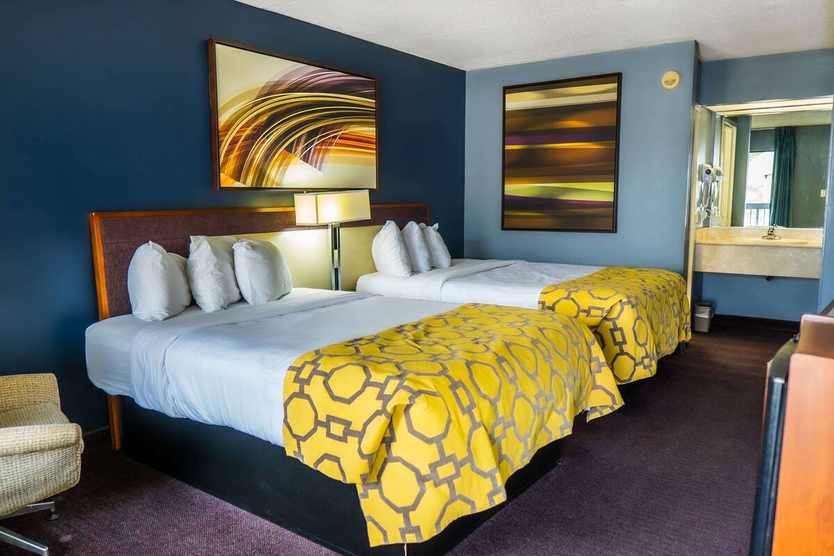 A hotel room with two beds, a large mirror, and artwork on the walls.
