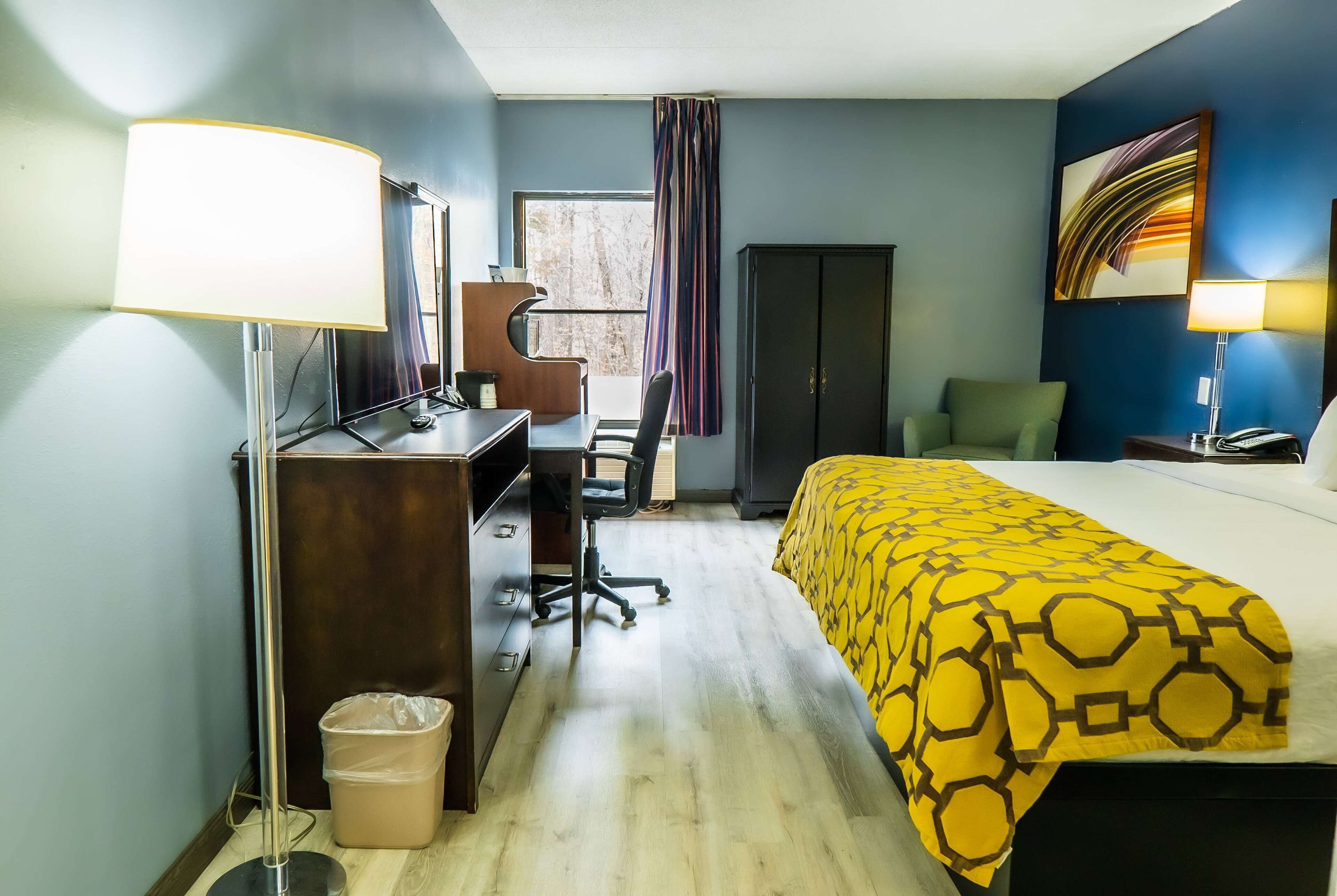 A hotel room with a bed, desk, chair, and a large window with curtains.