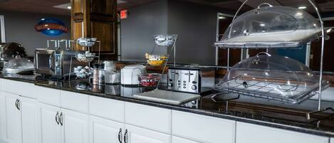 A breakfast bar with a coffee machine, toaster, and covered bowls of food.