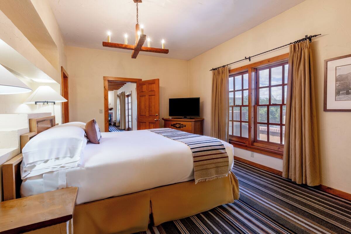 A hotel room with a large bed, a television, a wooden ceiling, and a window with curtains.
