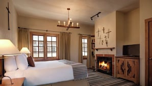 A hotel room with a large bed, a fireplace, a television, and a chandelier.