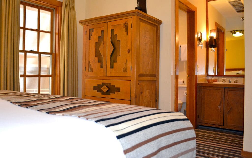 A hotel room with a bed, wooden wardrobe, and a bathroom with a mirror and sink.