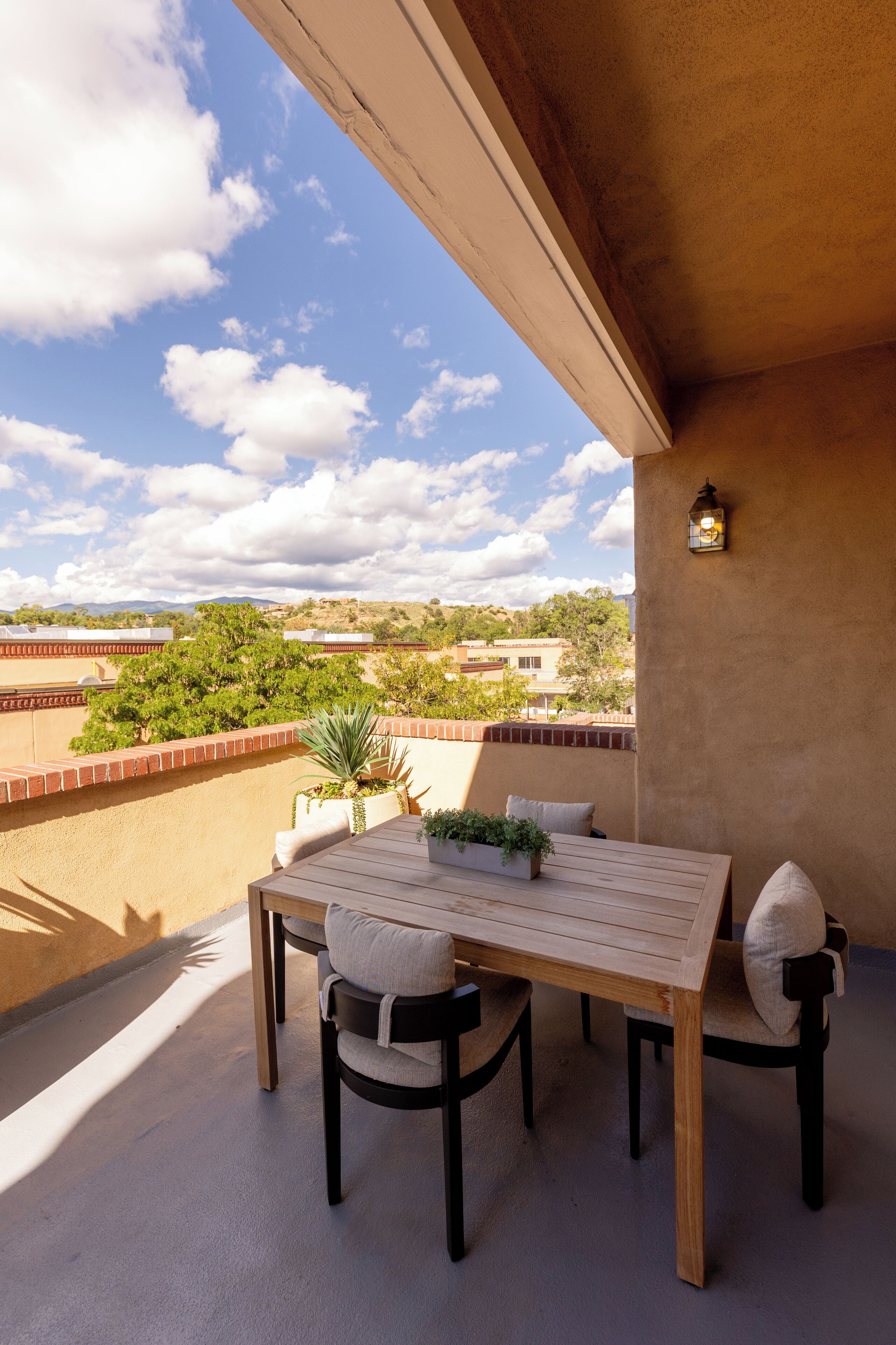 A balcony with a table and chairs, a potted plant, and a view of the landscape.
