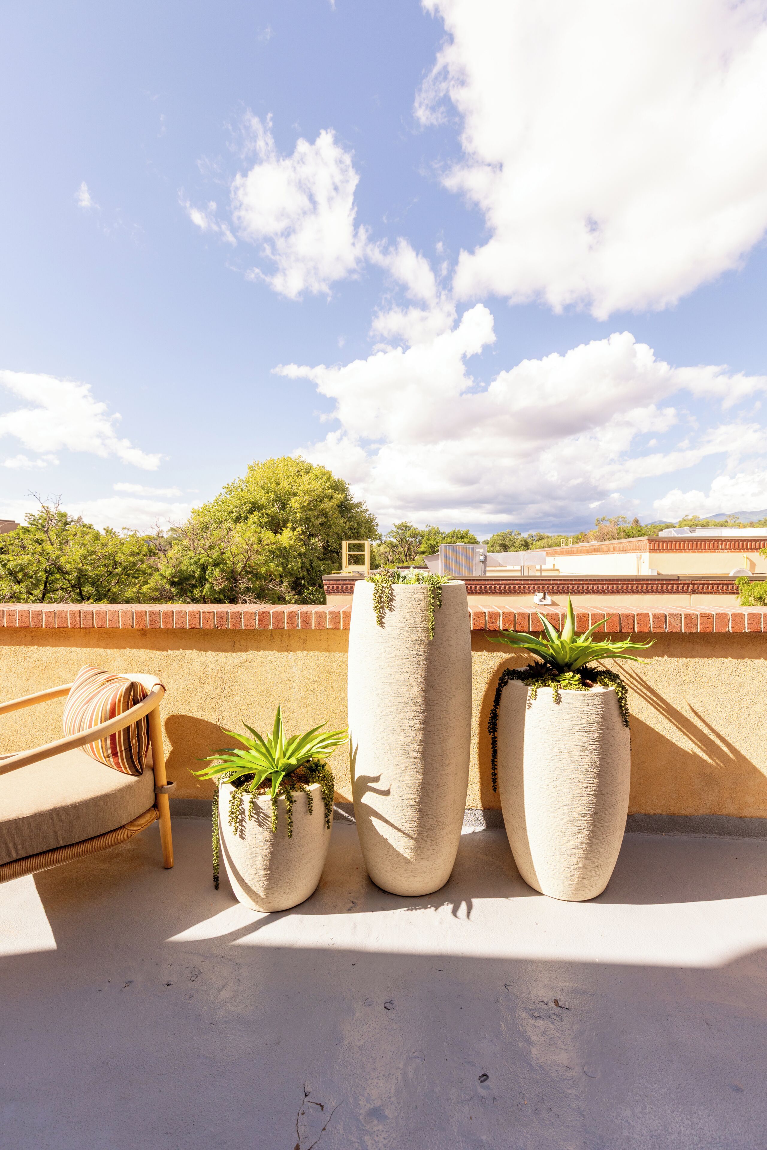Terraço no telhado com vista para a cidade, uma cadeira de madeira e dois grandes vasos com plantas.