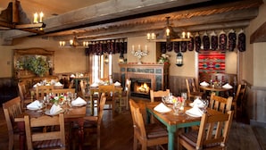 A restaurant with wooden tables and chairs, a fireplace, and hanging meats.