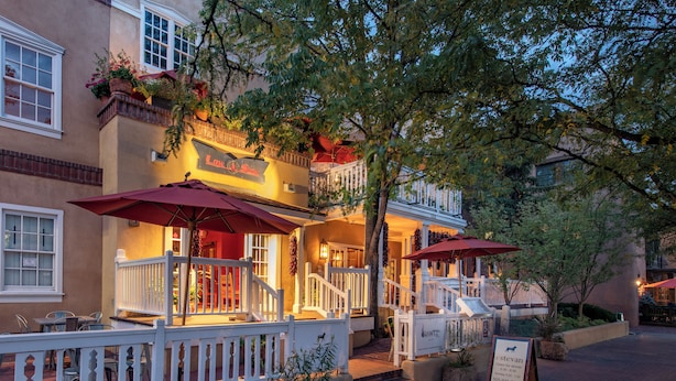 A restaurant with outdoor seating, a white fence, and a signboard.