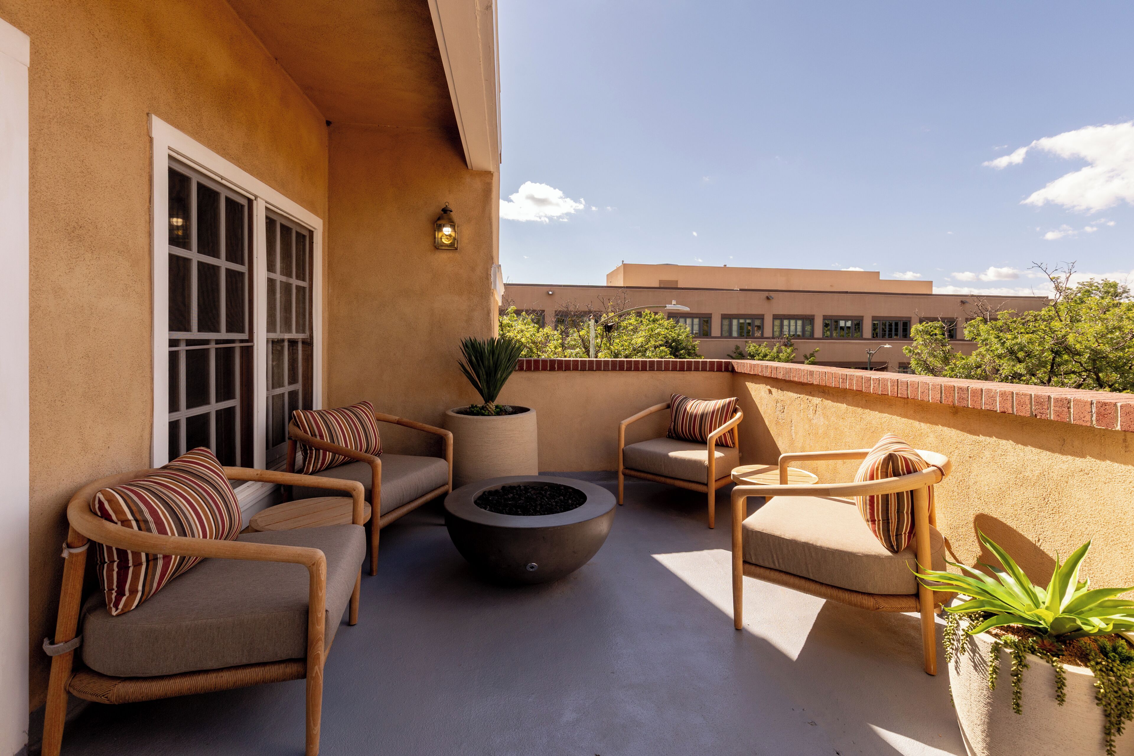 A balcony with outdoor seating, a fire pit, and a potted plant.