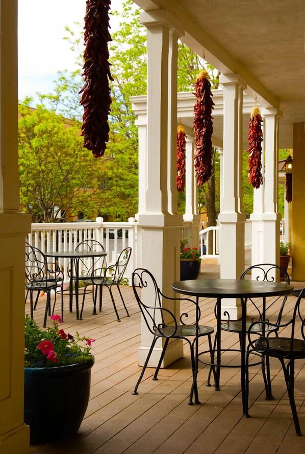 Un patio techado al aire libre con una mesa redonda y sillas, columnas blancas y pimientos rojos colgando.