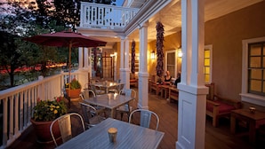 An outdoor patio with tables and chairs, a white railing, and hanging plants.