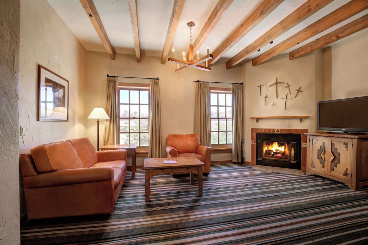 A living room with a fireplace, wooden beams, a sofa, a chair, and a television.