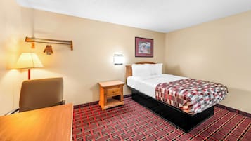 A hotel room with a bed, a desk, a chair, a nightstand, a lamp, and a wall-mounted shelf.