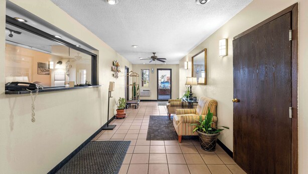 Eine Hotellobby mit einer Rezeption, einem Deckenventilator, einer Sitzecke mit Sesseln und einer großen Holztür.