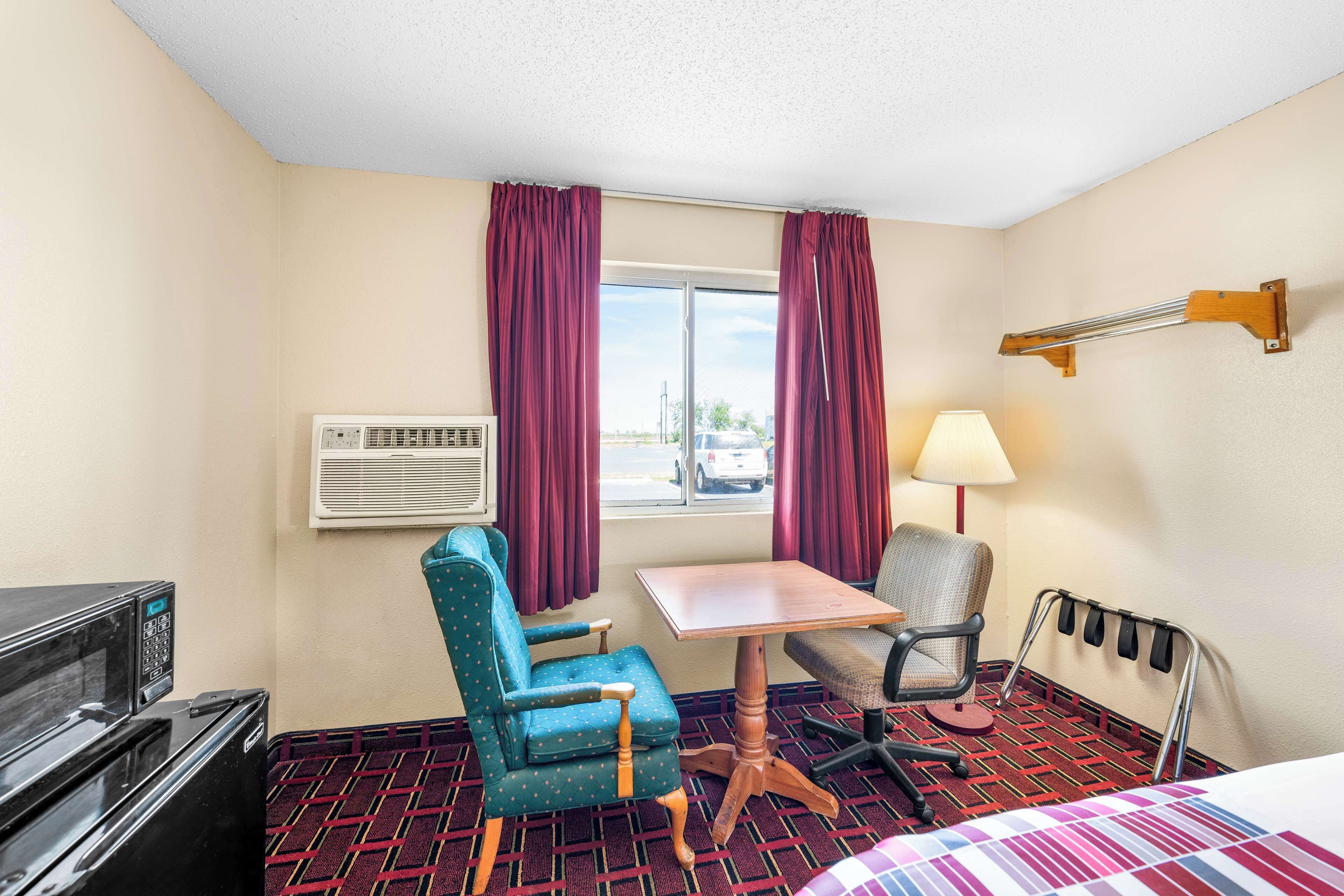 Une chambre d’hôtel comprenant un lit, un bureau, deux chaises, un appareil de climatisation, une lampe et une vue sur l’extérieur.