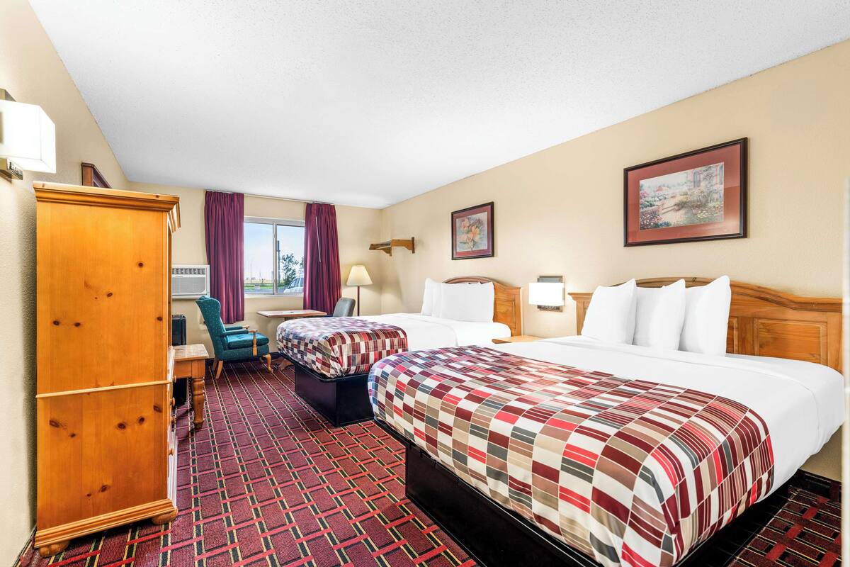 A hotel room with two beds, a wooden wardrobe, a desk, and a chair.