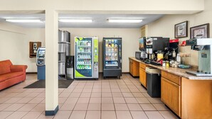 A kitchenette with a coffee machine, a microwave, and a refrigerator. There are vending machines and a sofa in the room.
