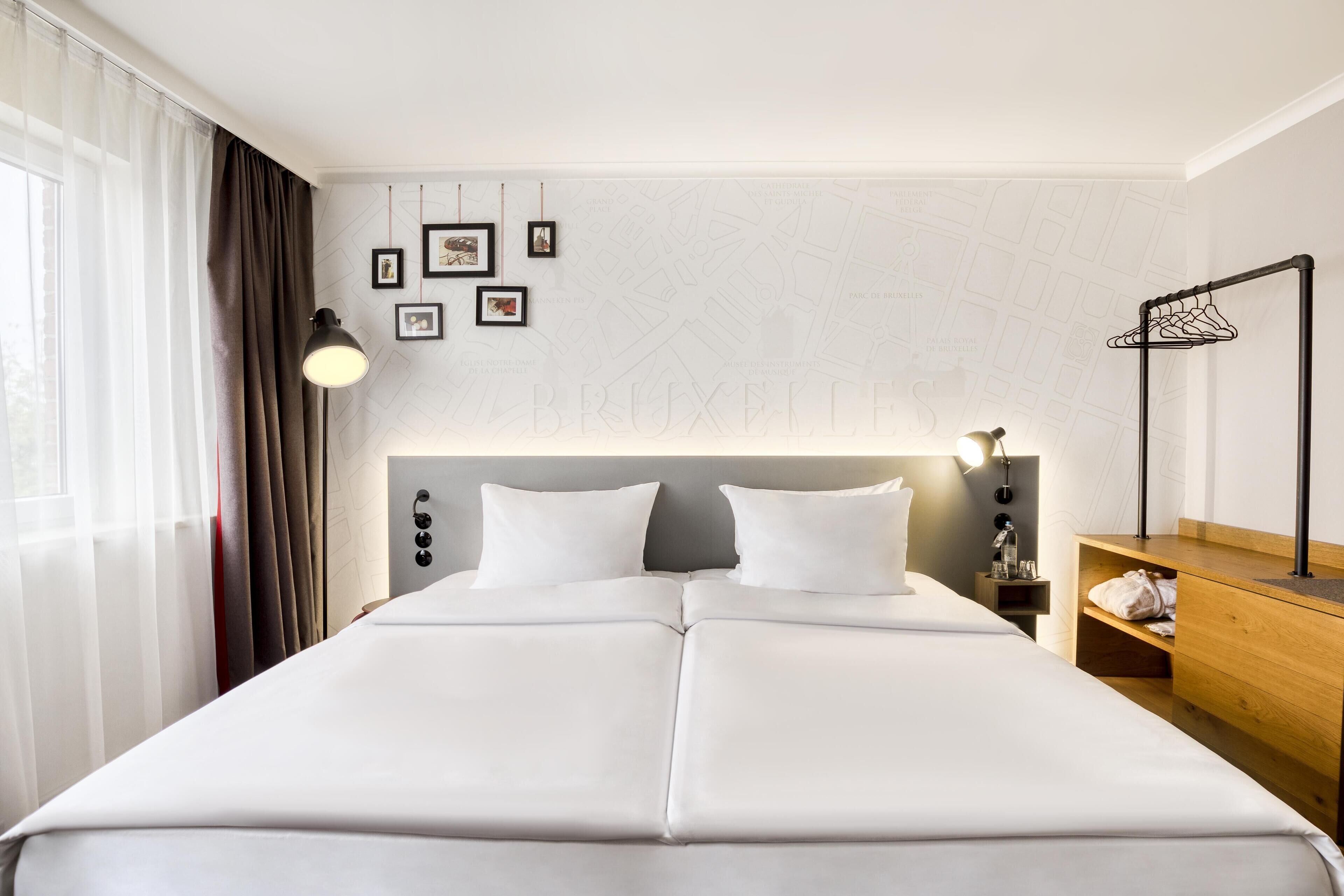Habitación de hotel con una cama grande, una mesita de noche con lámpara, una mesita auxiliar de madera y un mapa mural.