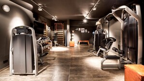 Un gimnasio con diverso equipo de ejercicio, un reloj en la pared y suelo de madera.