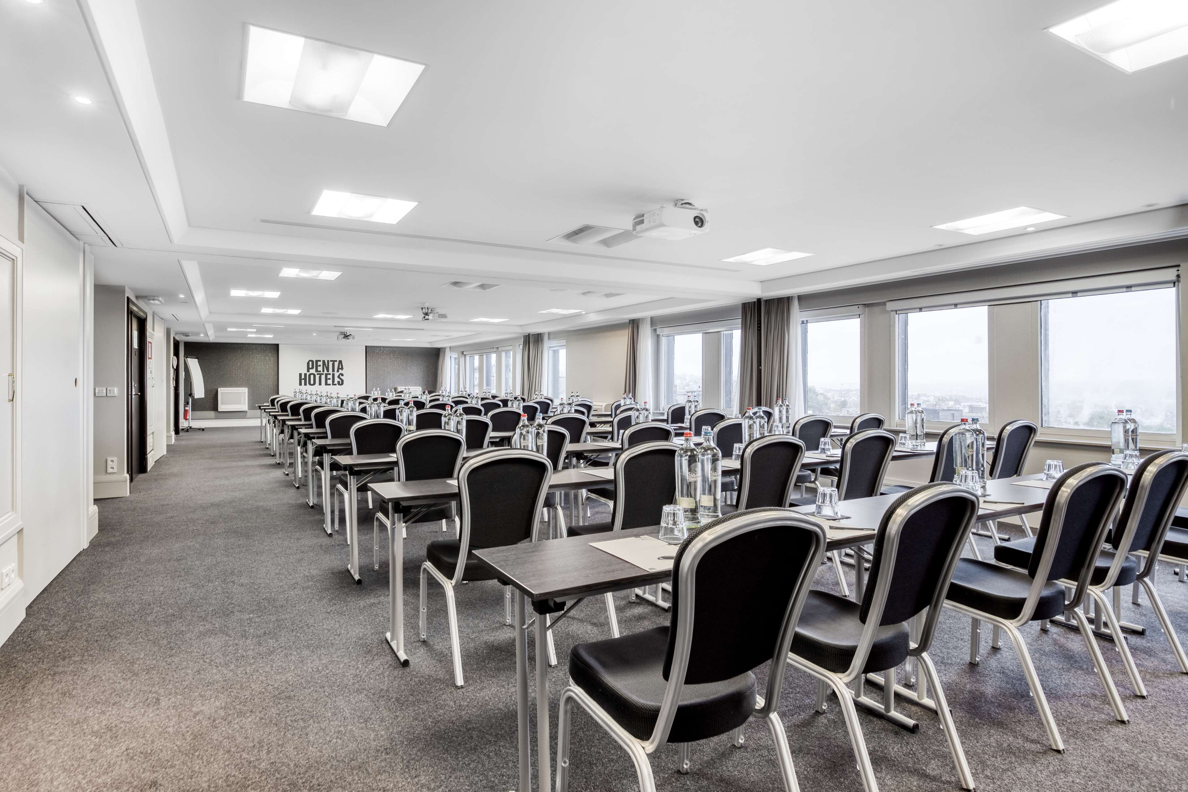 A conference room with rows of tables and chairs, large windows, and a sign for OENTA HOTELS.