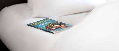 A neatly made bed with white linens and a single book placed on it.