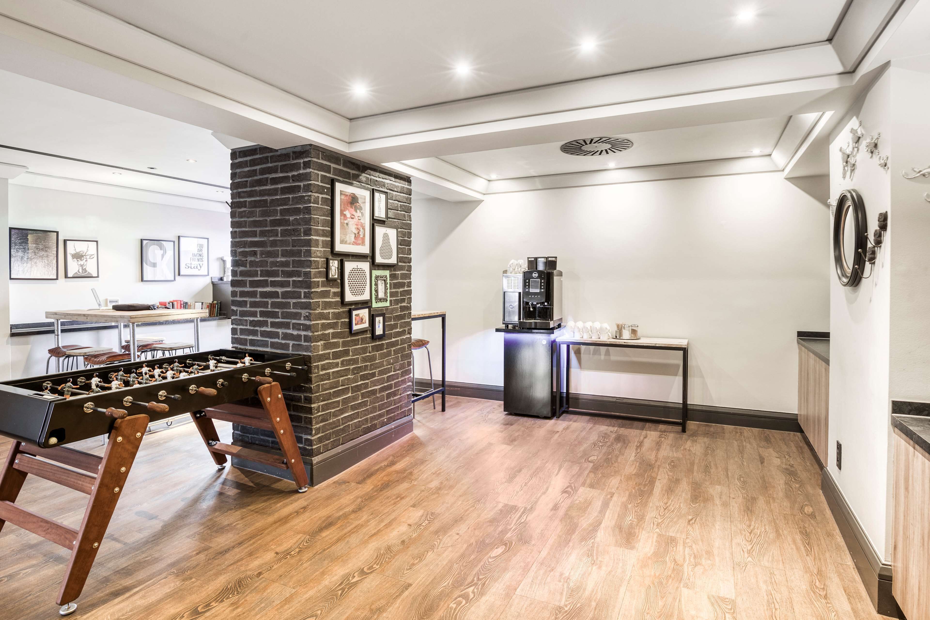 Una habitación moderna con una mesa de fútbol de mesa, una cafetera y una pared decorada con ladrillos.