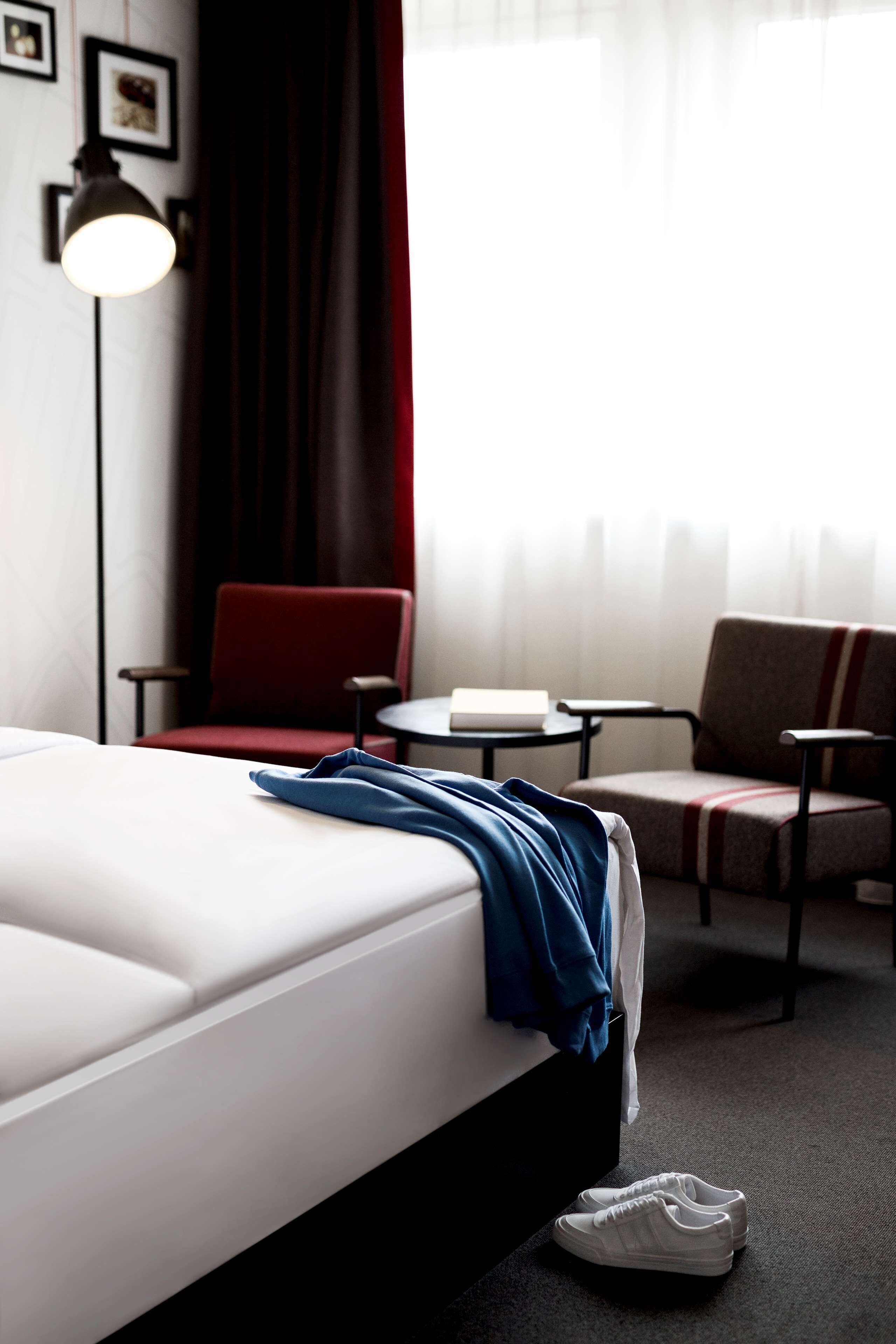 Une chambre d’hôtel avec un lit, deux chaises, une petite table et une lampe.
