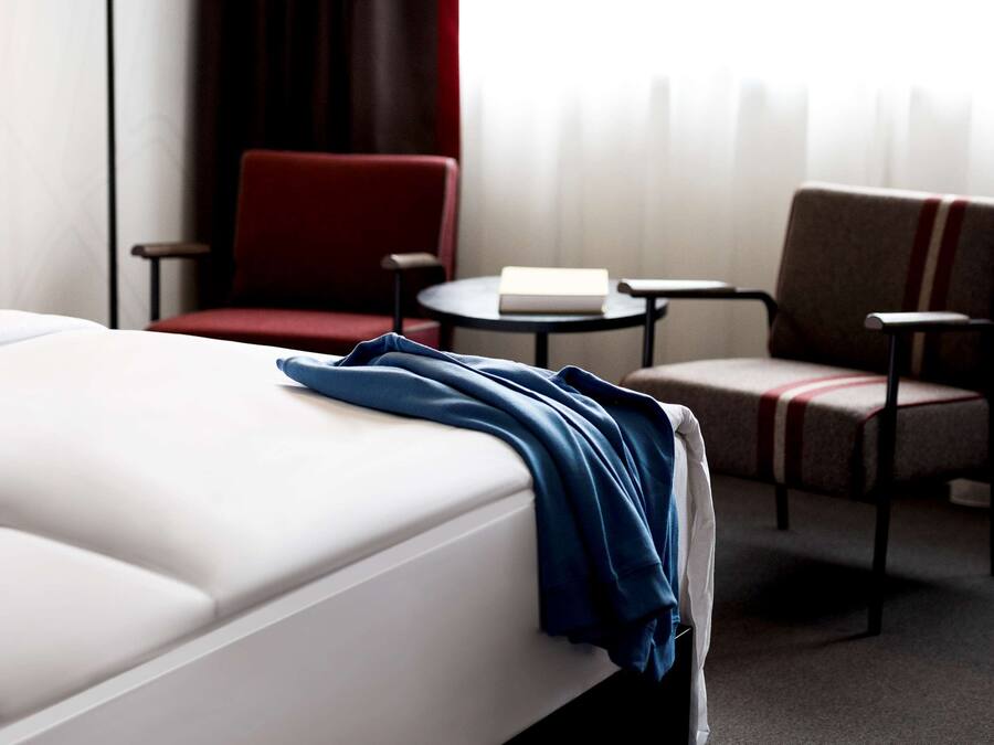Une chambre d’hôtel avec un lit, deux chaises, une petite table et une lampe.