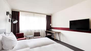 Habitación de hotel con dos camas, un escritorio, un televisor y una ventana con cortinas.