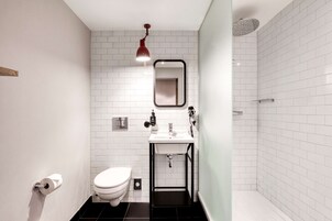 Un baño moderno con azulejos blancos tipo metro, un lavamanos negro, inodoro y zona de ducha.