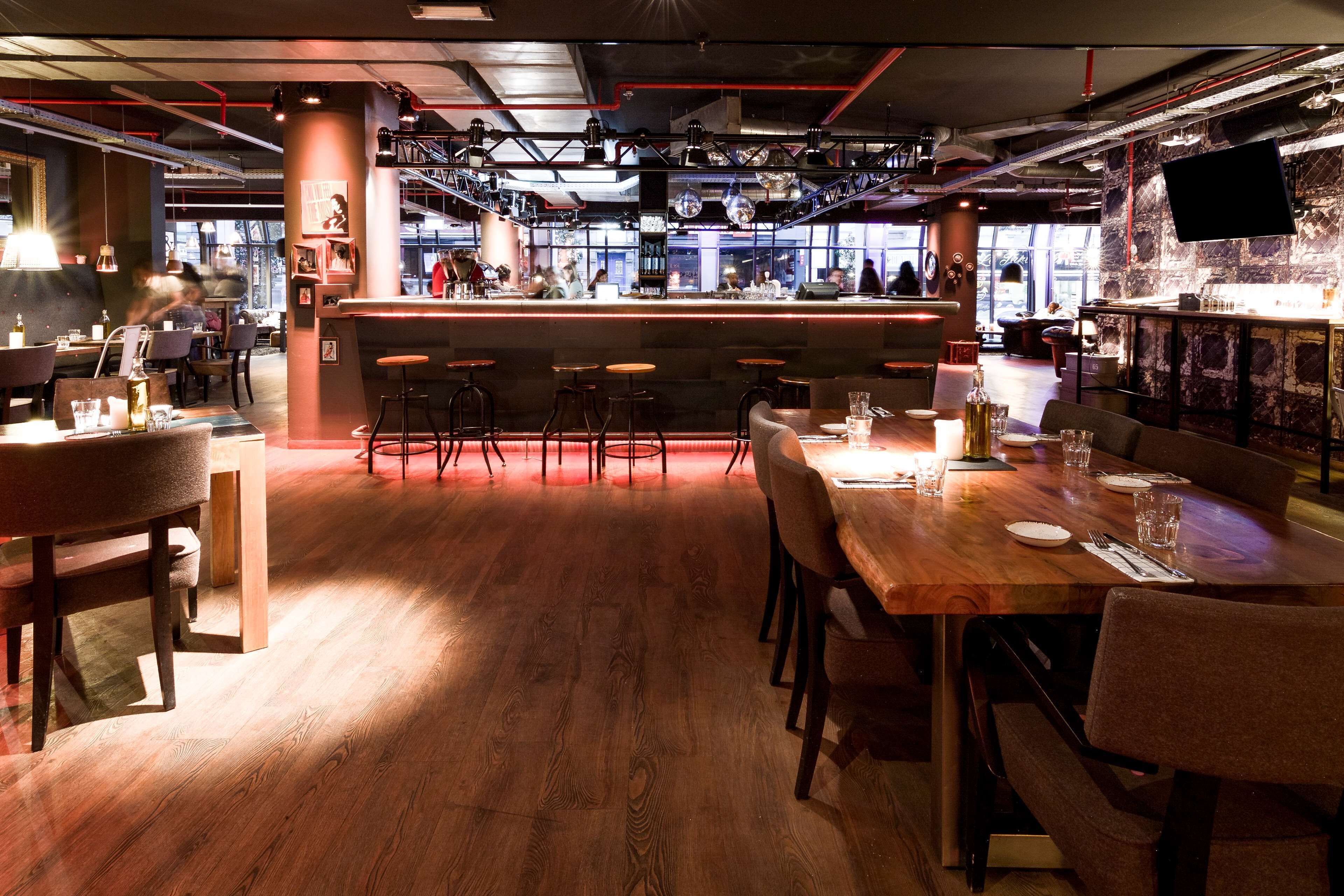 A modern restaurant with a bar area, wooden flooring, and bar stools.