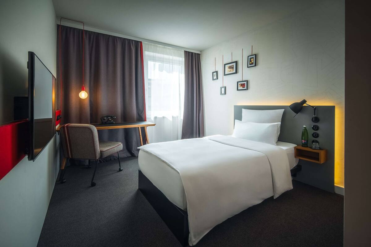 Une chambre d’hôtel avec un lit, un bureau, une chaise, une télévision et un mur orné de tableaux.