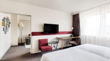 A hotel room with a bed, a desk, a chair, a TV, and a window with curtains.
