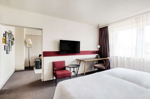 A hotel room with a bed, a desk, a chair, a TV, and a window with curtains.