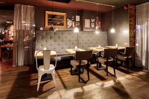 En restaurant med træborde og stole, en polstret bænk og en væg i mursten.